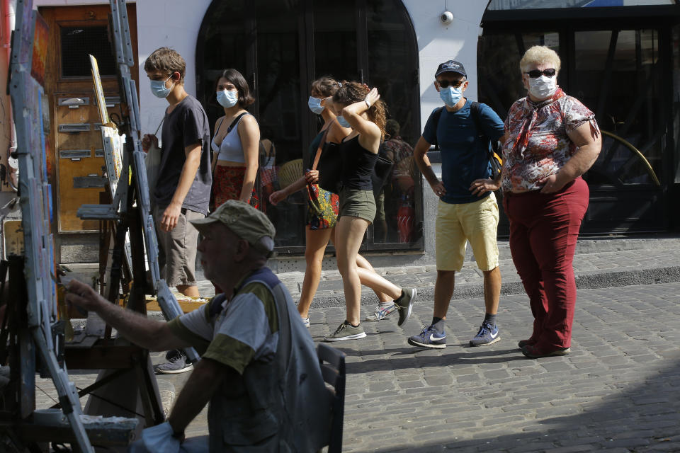 A fainter works while tourists stroll in the Montmartre district Monday, Aug. 10, 2020 in Paris. People are required to wear a mask outdoors starting on Monday in the most frequented areas of the French capital. The move comes as the country sees an uptick in virus infections. (AP Photo/Michel Euler)