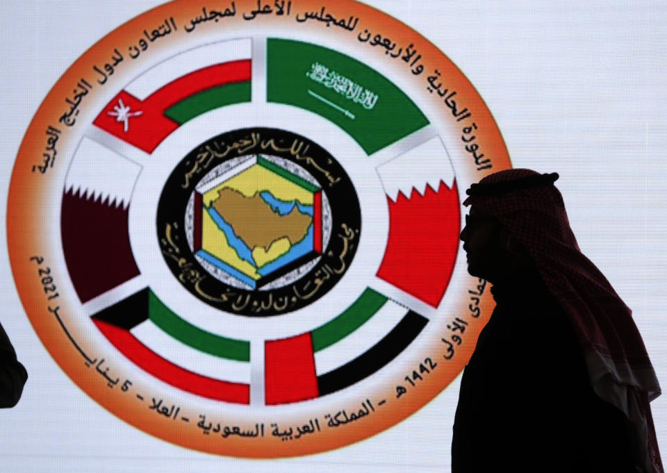 A Saudi television anchor stands in front of the logo of the 41st Gulf Cooperation Council (GCC) at the media center in at Al Ula, Saudi Arabia, Tuesday, Jan. 5, 2021. Kuwait's foreign ministry announced that Saudi Arabia will lift a years-long embargo on Qatar, opening its air and land borders in the first steps toward ending the Gulf crisis. (AP Photo/Amr Nabil)