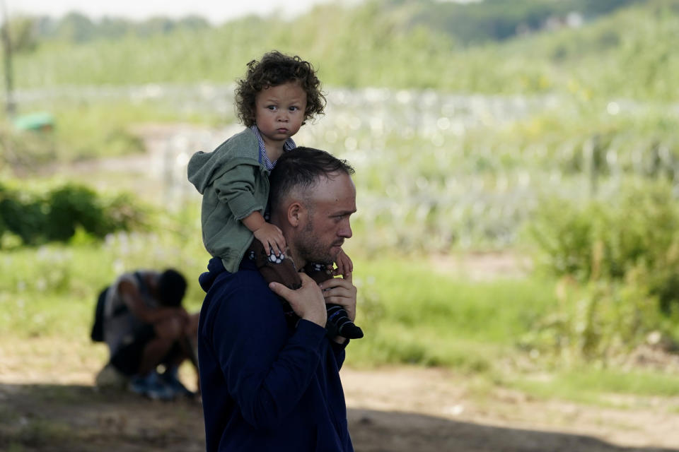 A man carries a child as they wait to be processed by the Border Patrol after illegally crossing the Rio Grande river from Mexico into the U.S. at Eagle Pass, Texas, Friday, Aug. 26, 2022. The area has become entangled in a turf war between the Biden administration and Texas Gov. Greg Abbott over how to police the U.S. border with Mexico. (AP Photo/Eric Gay)