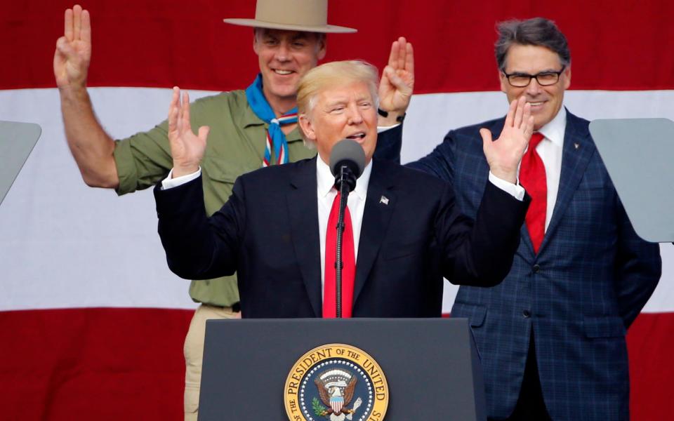 Donald Trump gestures as former boys scouts, Interior Secretary Ryan Zinke, left, Energy Secretary Rick Perry, watch at the 2017 National Boy Scout Jamboree - Credit: AP