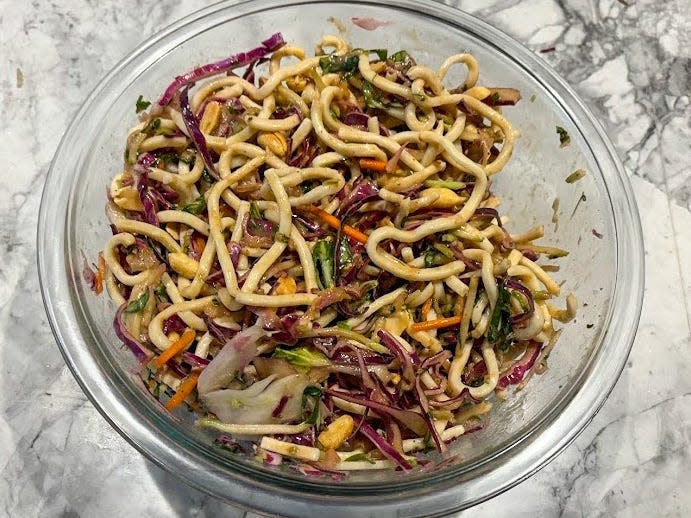 A pile of udon noodles, shredded cabbage, and carrots in a glass bowl on a gray tabletop