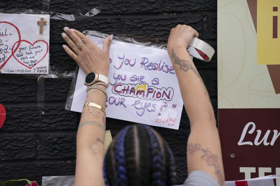 A woman tapes a message of support on a mural of Manchester United striker and England player Marcus Rashford, on the wall of the Coffee House Cafe on Copson Street, in Withington, Manchester, England, Tuesday July 13, 2021. The mural was defaced with graffiti in the wake of England losing the Euro 2020 soccer championship final match to Italy. (AP Photo/Jon Super)