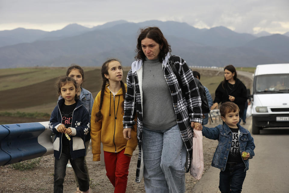 A woman and four children walk along a road with mountains in the distance.