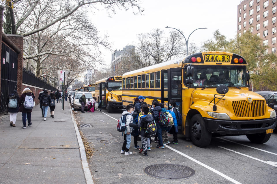Students wearing masks board a school bus outside New Explorations into Science, Technology and Math (NEST+m) school on the Lower East Side neighborhood of Manhattan on Tuesday, Dec. 21, 2021, in New York. (AP Photo/Brittainy Newman)