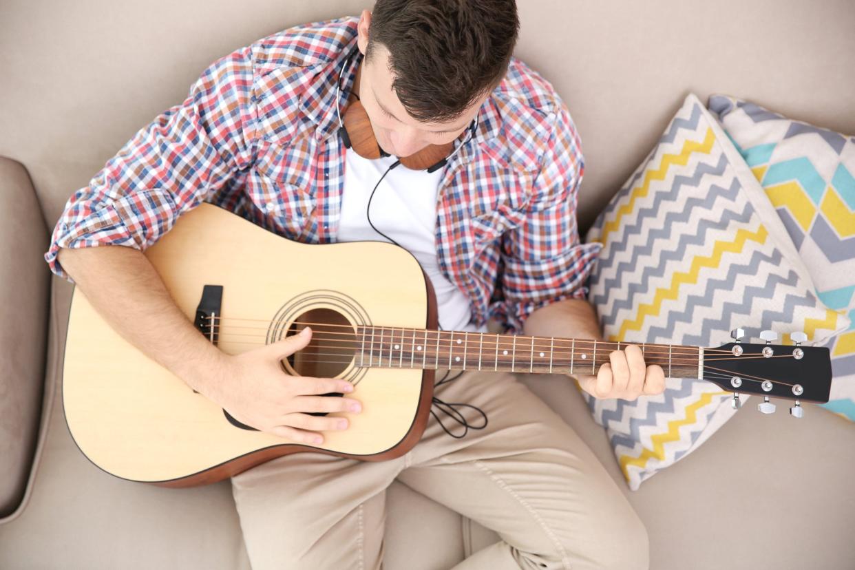 young man with headphones playing guitar and sitting on the couch