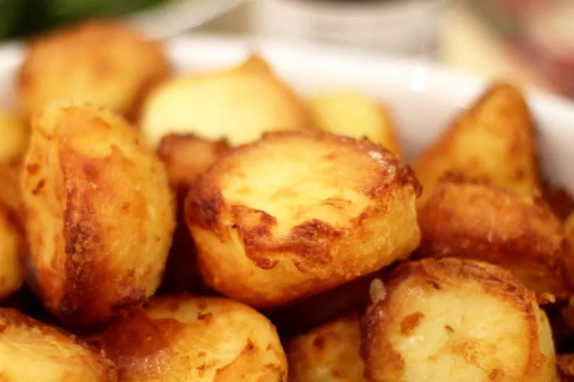 White dish served with golden roast potatoes piled high on top of each other. Out-of-focus background. Landscape orientation.