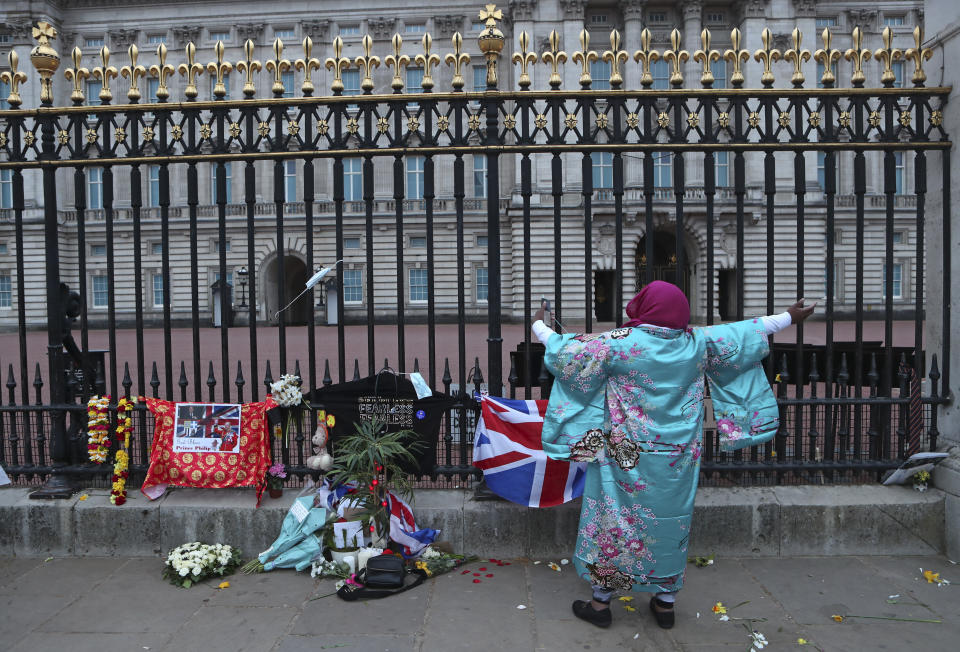 A woman gestures as she sings next to tributes left in honor of Britain's Prince Philip in front of Buckingham Palace in London on Saturday, April 10, 2021. Prince Philip, the irascible and tough-minded husband of Queen Elizabeth II who spent more than seven decades supporting his wife in a role that both defined and constricted his life, has died, Buckingham Palace said Friday. He was 99. (AP Photo/Tony Hicks)