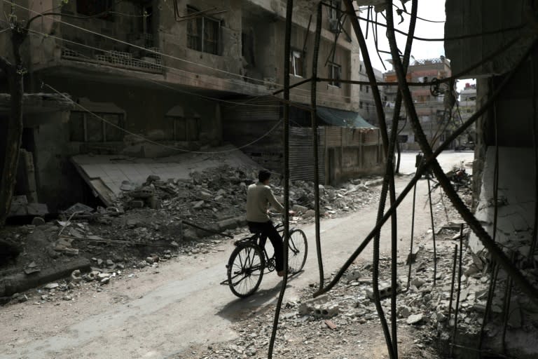 A Syrian rides his bicycle past a destroyed building in the Eastern Ghouta rebel-held enclave of Douma