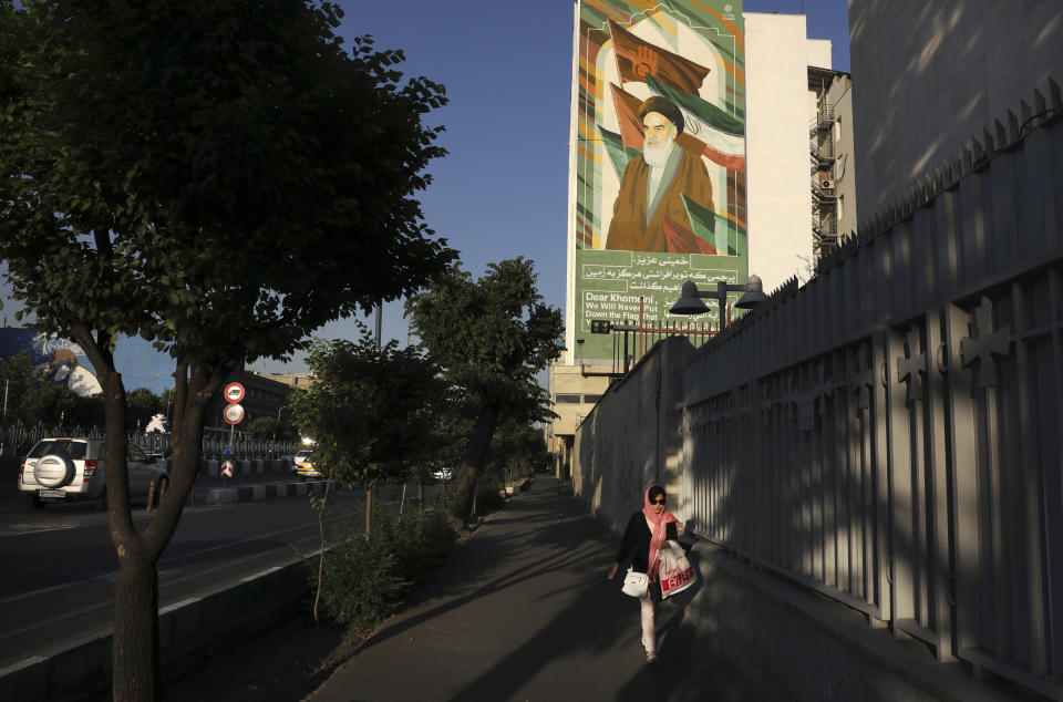 In this Saturday, May 18, 2019 photo, a woman walks past a mural of the late revolutionary founder Ayatollah Khomeini in Tehran, Iran. (AP Photo/Vahid Salemi)