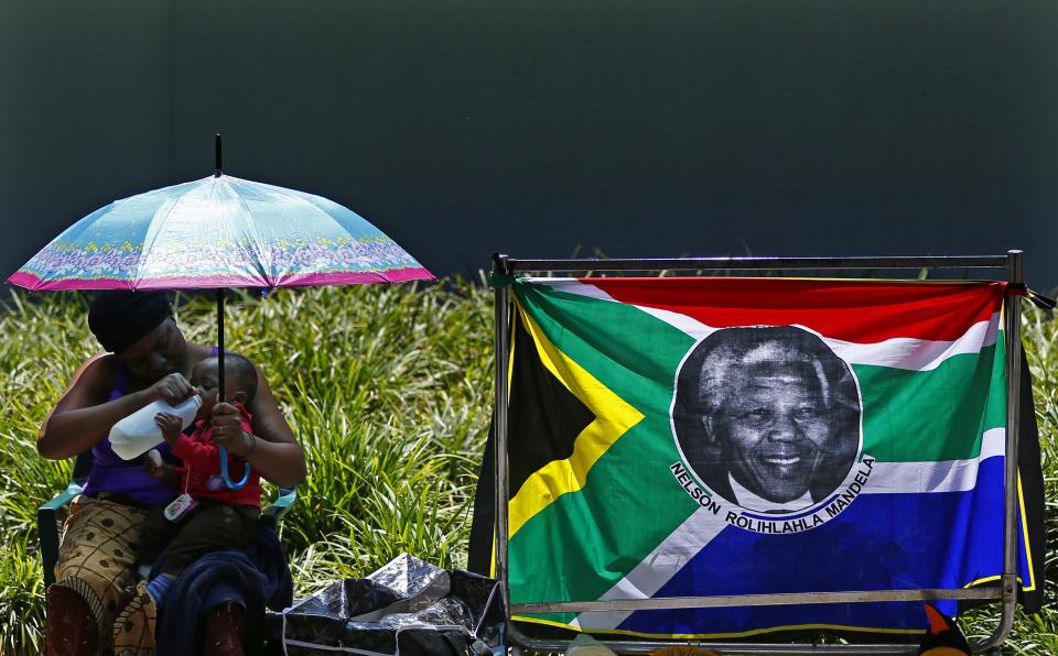 A woman gives water to her baby while sitting the house of former South African President Nelson Mandela in Johannesburg