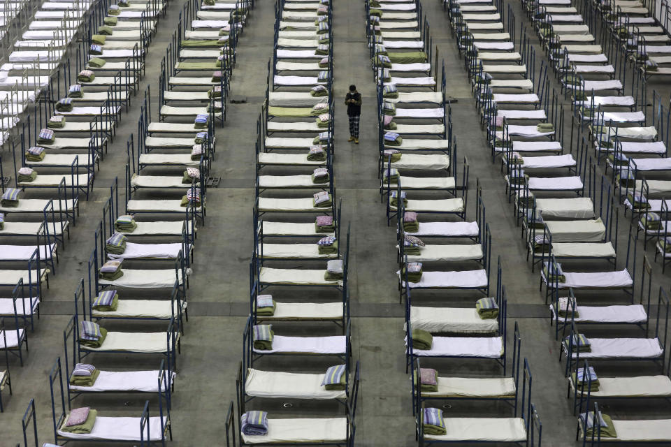 A worker walks among beds in a convention center that has been converted into a temporary hospital in Wuhan in central China's Hubei Province, Tuesday, Feb. 4, 2020. China said Tuesday the number of infections from a new virus surpassed 20,000 as medical workers and patients arrived at a new hospital and President Xi Jinping said "we have launched a people's war of prevention of the epidemic." (Chinatopix via AP)