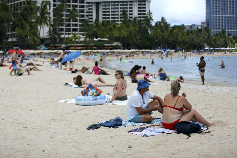 Brett Walsh and Emma Yates, bottom right, tourists from Australia, sit on Waikiki Beach in Honolulu, Monday, May 23, 2022. A COVID surge is under way that is starting to cause disruptions as schools wrap up for the year and Americans prepare for summer vacations. Case counts are as high as they've been since mid-February and those figures are likely a major undercount because of unreported home tests and asymptomatic infections. But the beaches beckoned and visitors have flocked to Hawaii, especially in recent months. (AP Photo/Caleb Jones)