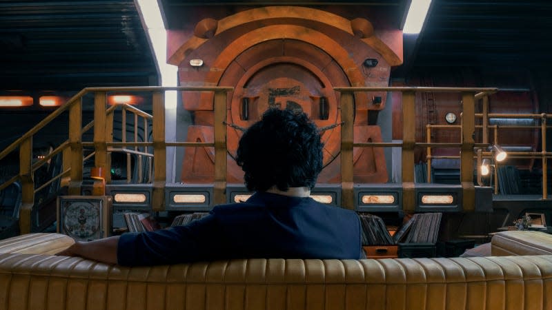Spike Spiegel sits on a couch in his spaceship, facing away from the camera.