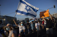 Israeli social workers wave a national flag as they block a main road during a protest against the economic situation in the central Israeli town of Kfar Ahim, Thursday, July 9, 2020. With a new outbreak of coronavirus devastating Israel's economy, one of Prime Minister Benjamin Netanyahu's closest confidants was dispatched on to a TV studio on a recent day to calm the nerves of a jittery nation. Instead, he dismissed the public's economic pain as "BS." (AP Photo/Sebastian Scheiner)