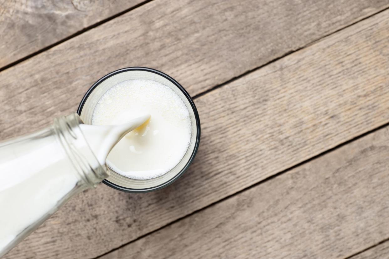 top view of milk pouring from bottle into glass on old wooden table