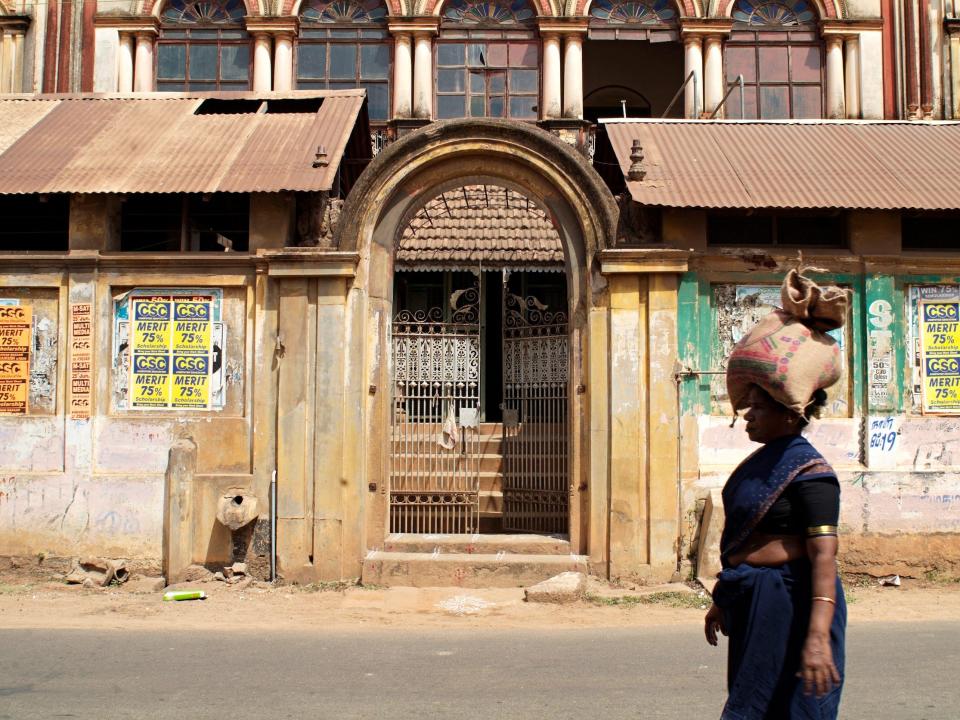 A woman with a brown sack atop her head walks past a derelict Chettinad mansion in 2006.