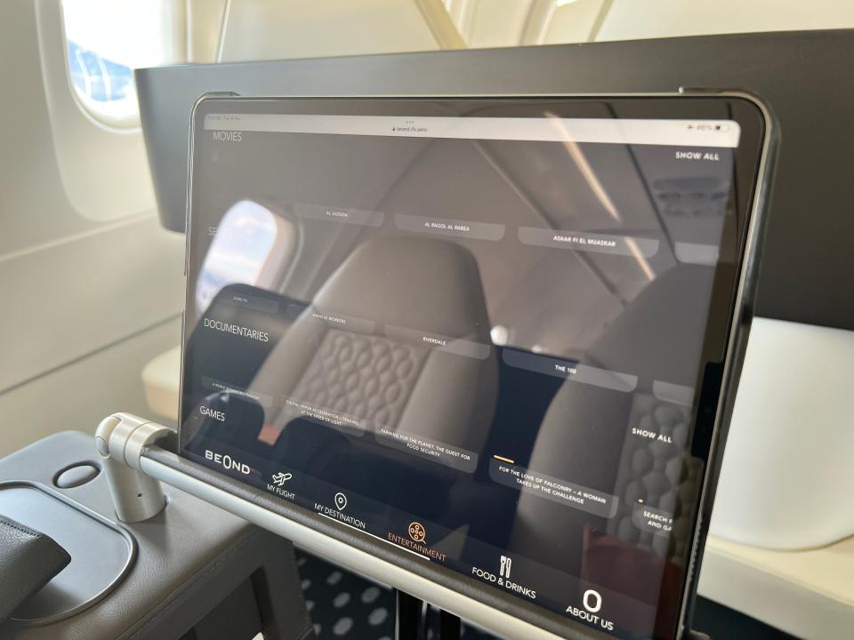 An iPad onboard a Beond airliner shows text descriptions of movies and tv shows, but no images