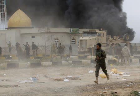 A Shi'ite fighter known as Hashid Shaabi, runs as smoke rises from an explosives-laden military vehicle driven by an Islamic State suicide bomber which exploded during an attack on the southern edge of Tikrit March 12, 2015. REUTERS/Thaier Al-Sudani