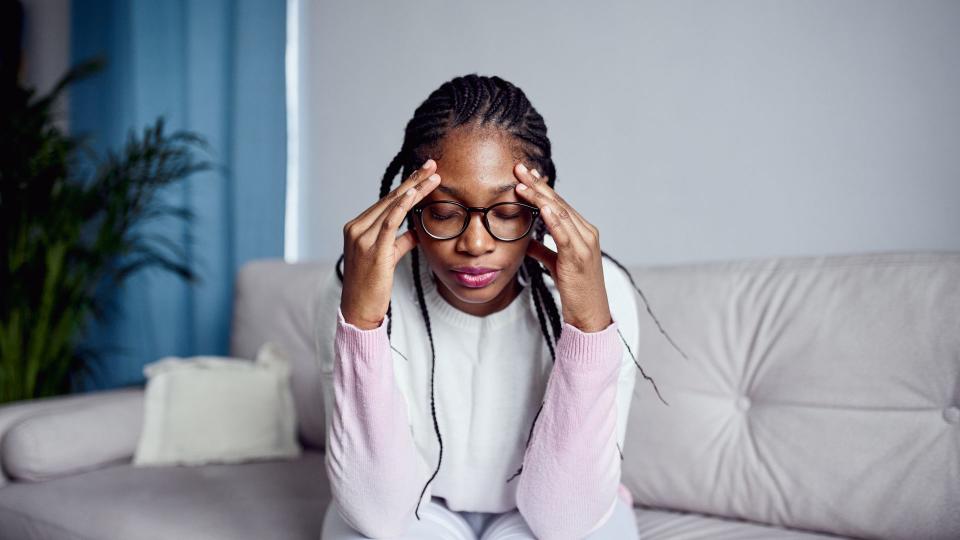 A young woman is sitting on the sofa at home with her head in her hands. The concept of health problems , headache or stress