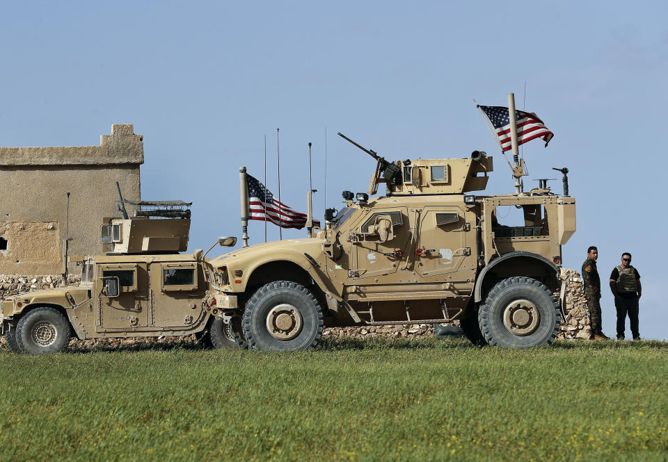 FILE - In this file picture taken on Thursday, March 29, 2018, a fighter, second from right, of U.S-backed Syrian Manbij Military Council stands next to U.S. humvee at a U.S. troop's outpost on a road leading to the tense front line between Syrian Manbij Military Council fighters and Turkish-backed fighters, at Halawanji village, north of Manbij, Syria. A spokesman for the U.S.-led coalition said Friday, Jan. 11, 2019 that the process of withdrawal in Syria has begun, declining to comment on specific timetables or movements. (AP Photo/Hussein Malla, File)