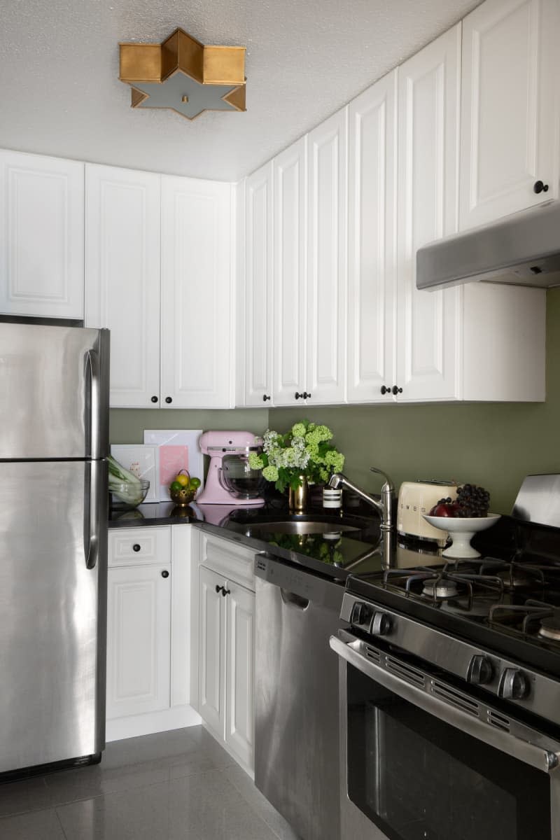 White cabinets in kitchen with green backsplash and black counter tops