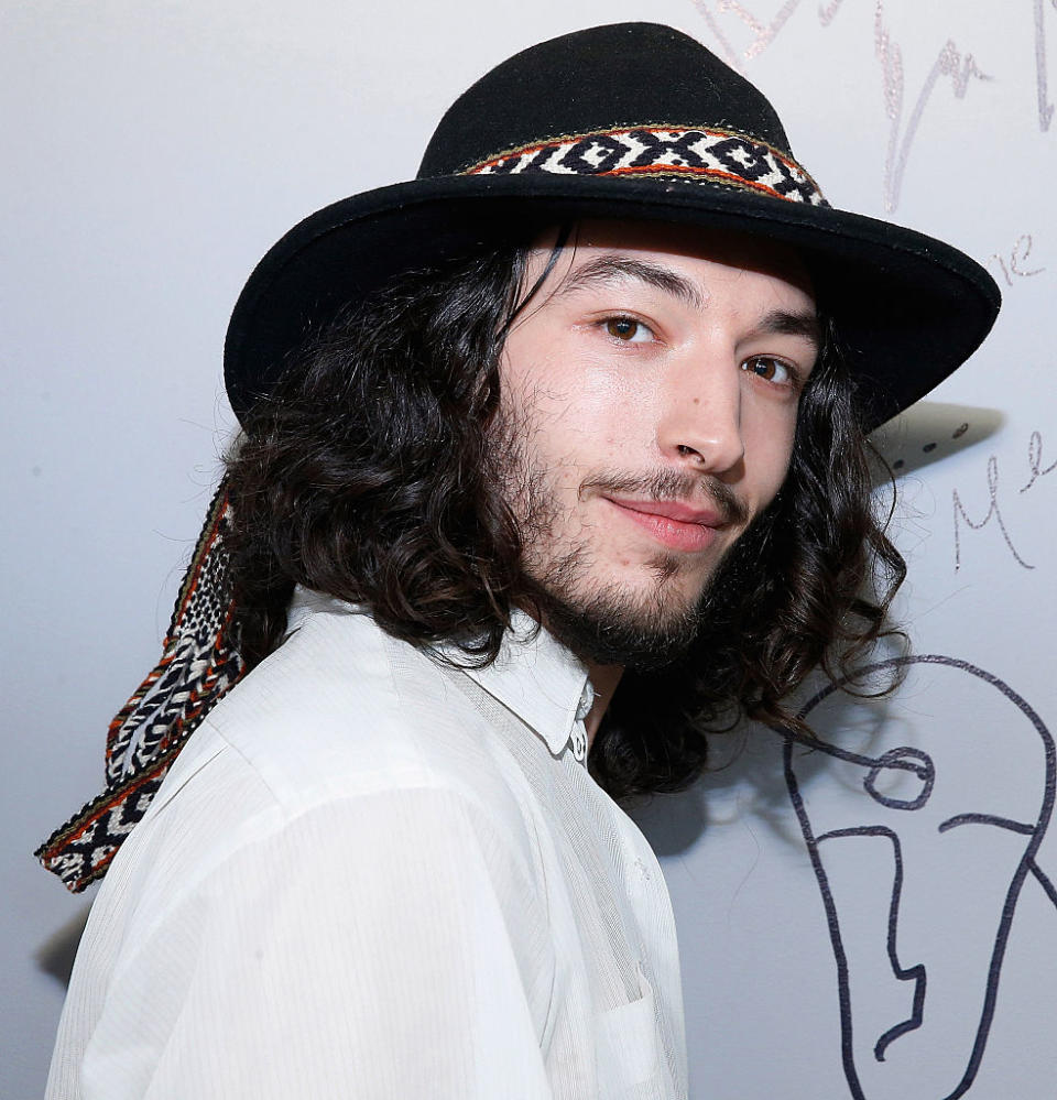 Ezra in a white shirt and black hat with patterned band posing for photo