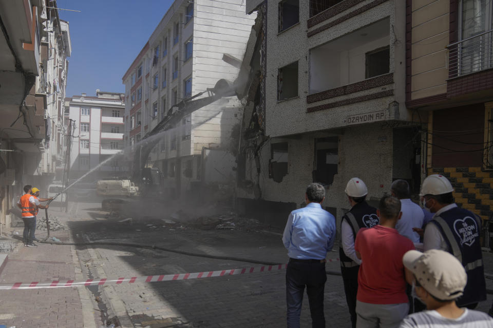 People on a side watch an excavator demolishing an old apartment building in Istanbul, Turkey, Friday, Aug. 4, 2023. Six months ago today, a devastating 7.8-magnitude earthquake hit the Kahramanmaras and 10 other provinces in southern Turkey on the morning of February 6th. Over 50,000 people died, and hundreds of thousands were left homeless, sheltering in tents and other temporary accommodation. (AP Photo/Khalil Hamra)