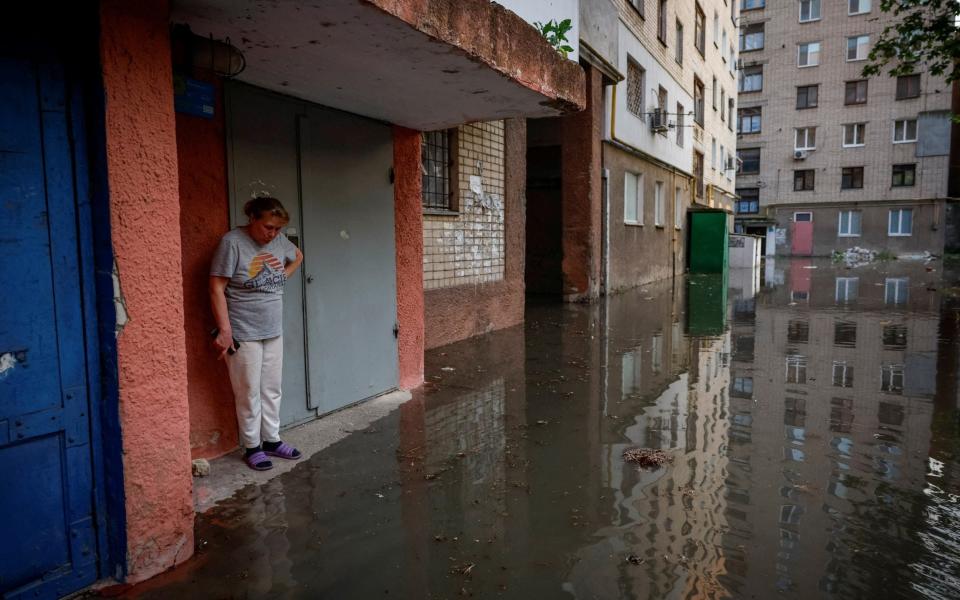 Olena stands next to the entrance to her house on a flooded street in Kherson - ALINA SMUTKO/REUTERS