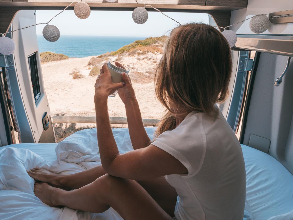 Road trip concept, woman living the van life experience watching stunning view while lying on the bed of the back of her camper
