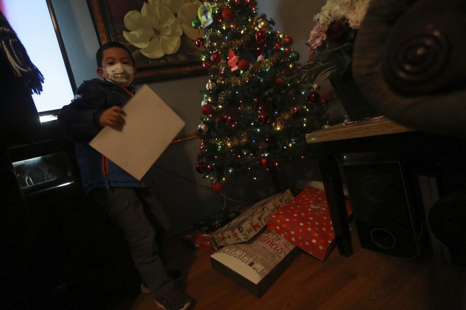 Angel, 6, shows an unopened Christmas present from his uncle on Wednesday, Dec. 23, 2020, in Santa Fe, N.M. Angel's parents, both cooks, struggled to pay rent this year as their hours were cut in half. His mother Angelica Rodriguez told him Santa wouldn't visit the house this year because they caught COVID-19. She says payments from a city relief program have allowed her family to make rent this year. (AP Photo/Cedar Attanasio)