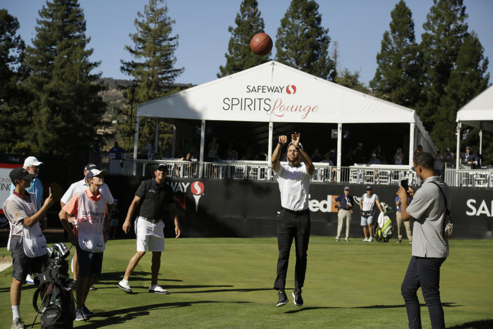 Stephen Curry shoots a basketball from the 17th green of the Silverado Resort North Course as Phil Mickelson watches during the pro-am for the Safeway Open PGA golf tournament Wednesday, Sept. 25, 2019, in Napa, Calif. (AP Photo/Eric Risberg)