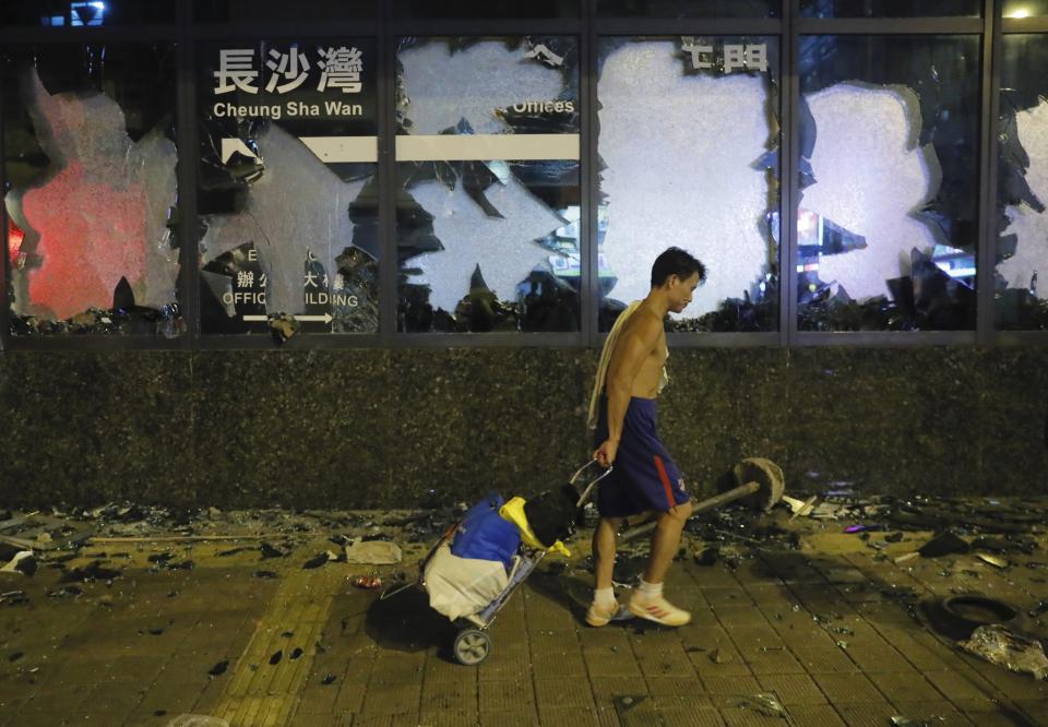 A pedestrian walks past a vandalized building in Hong Kong, Tuesday, Oct. 1, 2019. A Hong Kong police official says a pro-democracy protester was shot when an officer opened fire with his revolver during clashes Tuesday. A video of the incident, shot by the City University Student Union and shared on social media, shows a dozen black-clad protesters hurling objects at a group of riot police pursuing them. One officer, who was surrounded, drew his revolver and pointed it at the group. He fired and one protester collapsed on the street while others fled. (AP Photo/Kin Cheung)