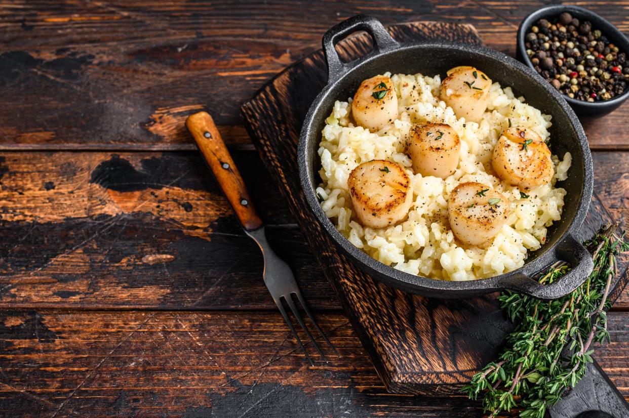 Seafood Risotto with Scallops in a pan. Dark wooden background. Top view. Copy space.