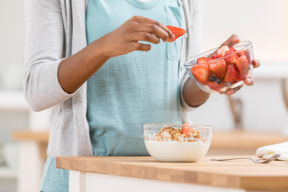 Person placing strawberries into a bowl of yogurt and granola