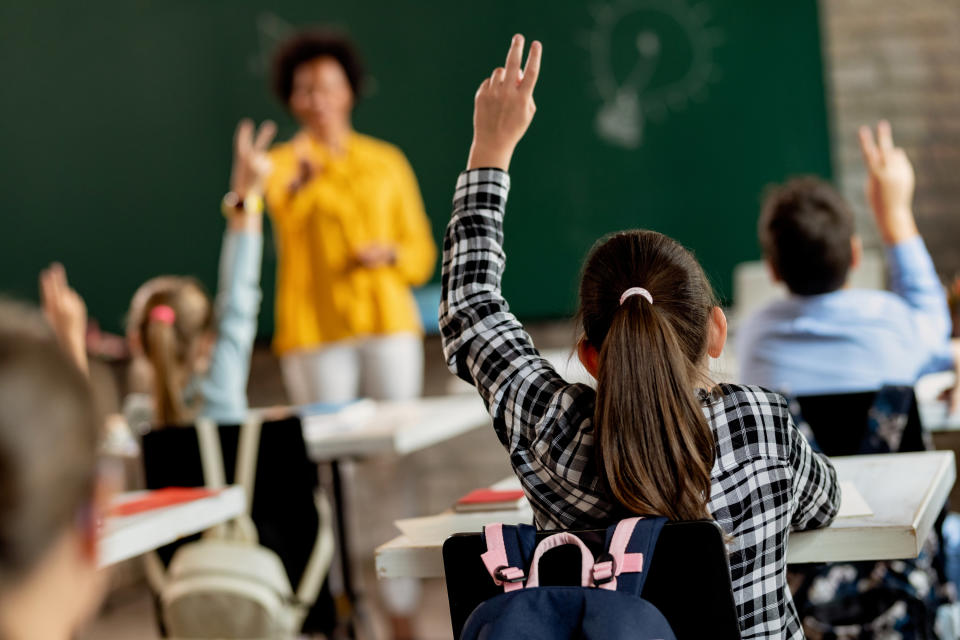 back view of elementary students raising their hands to answer questions