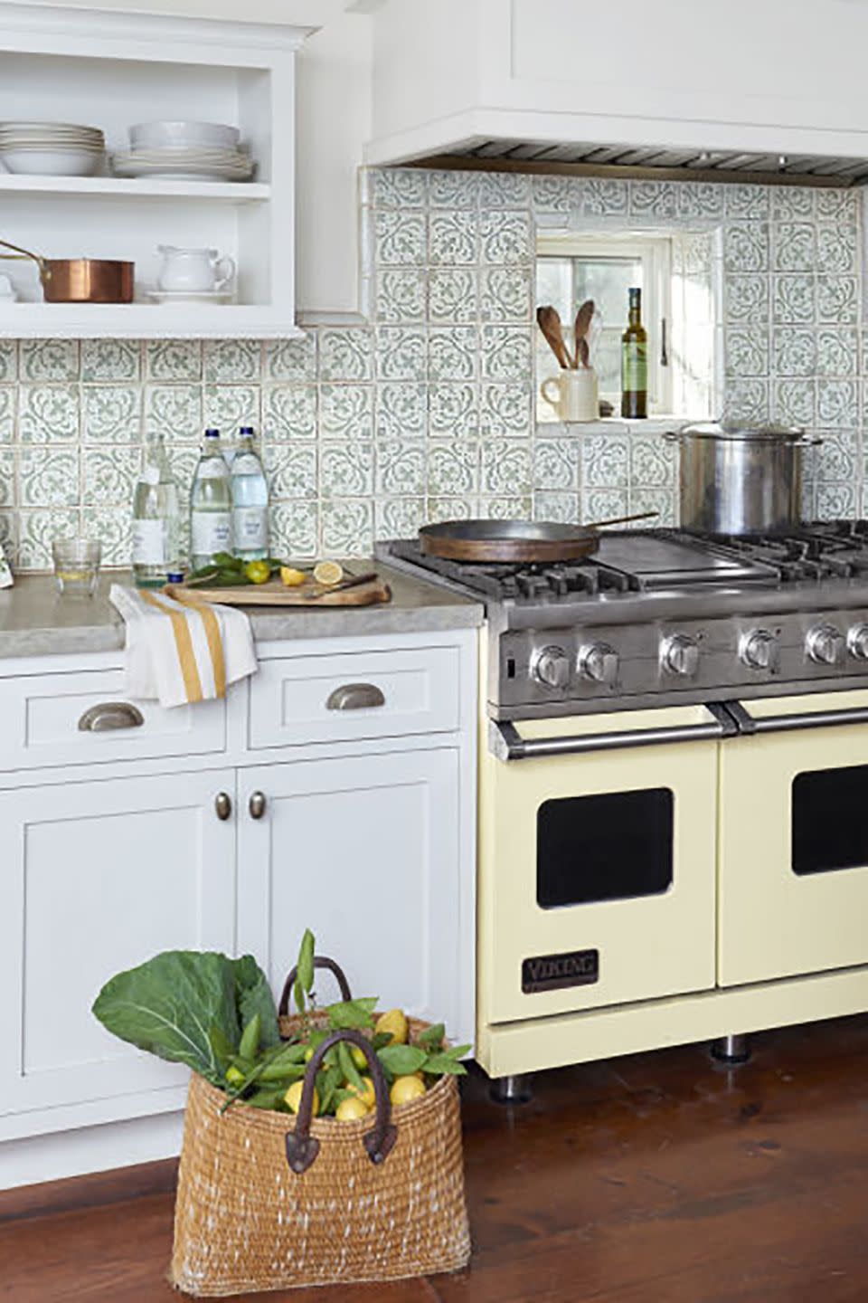 a butter yellow stove sits against a white and green tile backsplash and white cabinets and concrete countertops