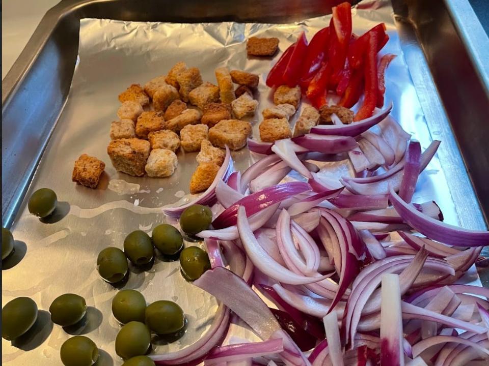 Olives, onions, croutons, and peppers on foil.