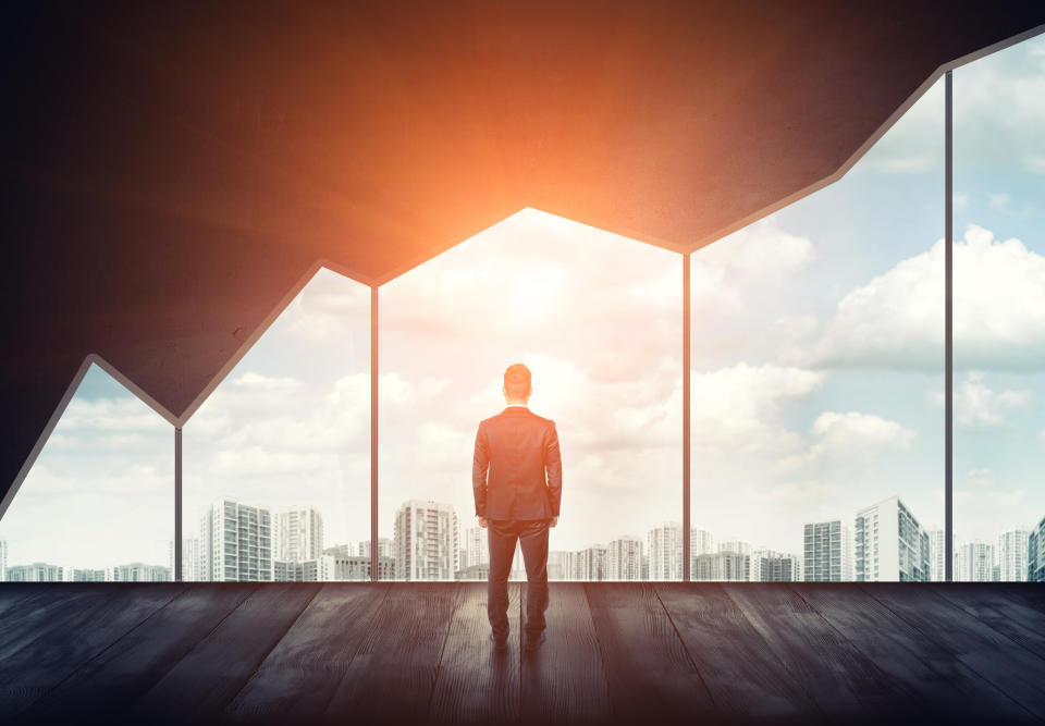 Man in suit overlooking a cityscape with windows that resemble a rising stock-market chart.