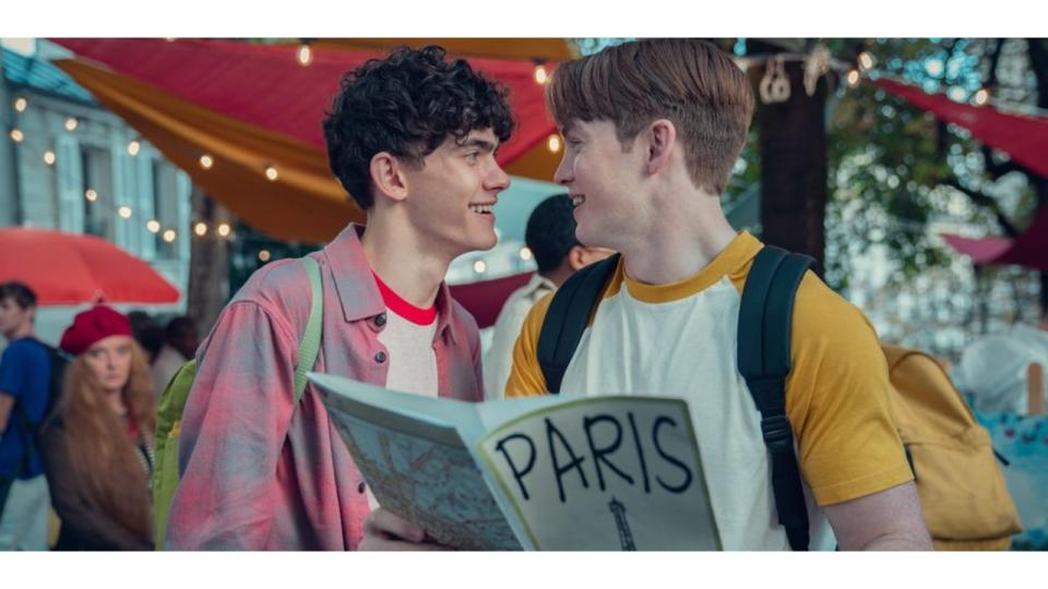 Charlie and Nick grinning at each other, Nick is holding a map of Paris