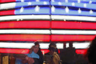 People embrace inside a coffee shop as a U.S. flag is reflected by the store's window Thursday, March 12, 2020, in Times Square in New York. Broadway theaters were shuttered Thursday after New York Gov. Andrew Cuomo banned gatherings of more than 500 people amid a rise in coronavirus cases. (AP Photo/Kathy Willens)