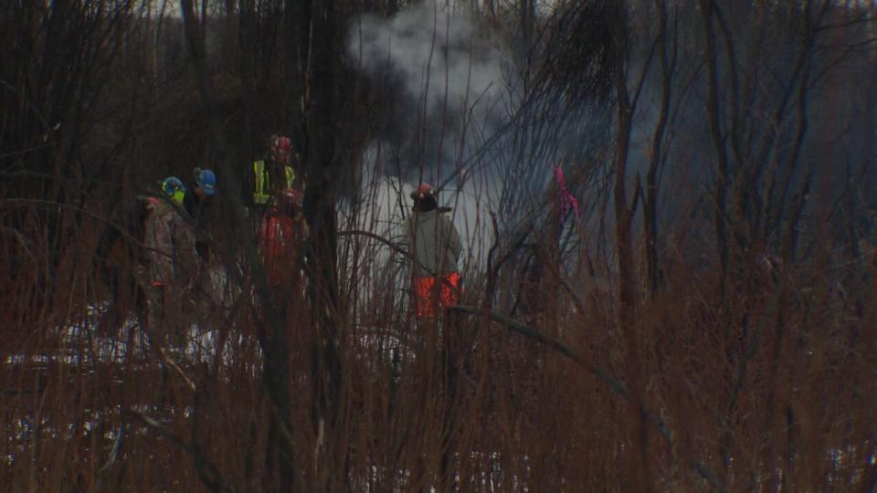 Provincial firefighters dressed in bunker gear scout the area of Fox Lake, near High Level, Alta., to map out wildfire hotspots and dig up carryover ground fires.