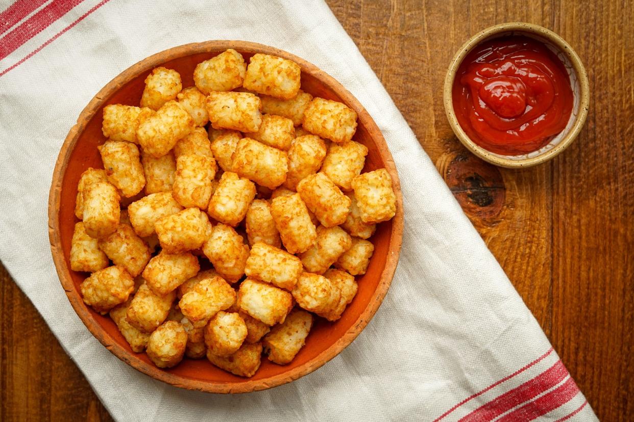A wooden bowl of homemade tater tots on a red striped white napkin with a small bowl of ketchup on a rustic wooden table