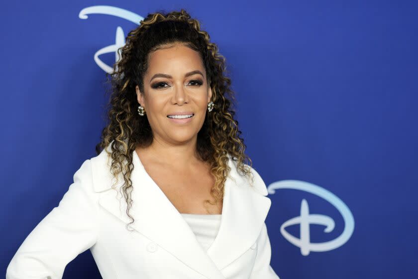 A woman with curly hair poses in a white suit