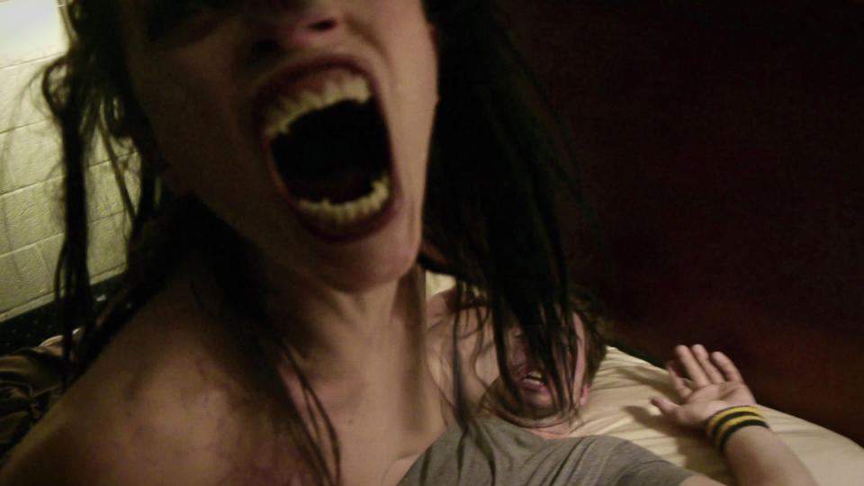 A still from VHS Amateur Night shows a woman with sharp teeth opening her mouth above a screaming man
