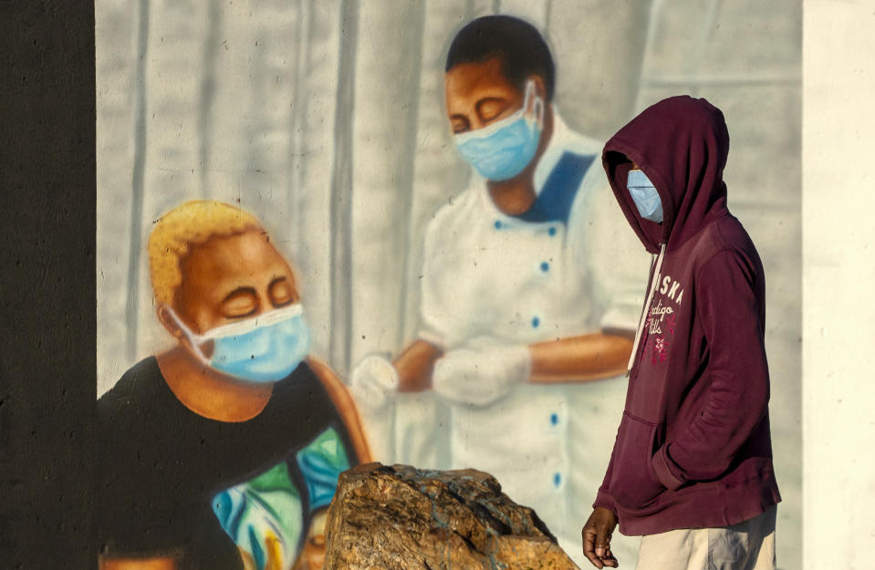 A man wearing a face mask to prevent the spread of coronavirus, walks past a mural promoting COVID-19 vaccinations in Duduza township, east of Johannesburg, South Africa, Wednesday, June 23, 2021. A survey of people aged 18-24 in 15 African countries found that many have lost jobs or have seen their education disrupted by the pandemic. (AP Photo/Themba Hadebe)