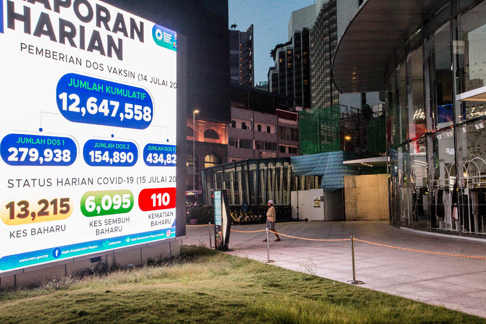 A pedestrian walks past a digital screen displaying the new daily record of Covid-19 cases in Kuala Lumpur July 15, 2021. — Picture by Firdaus Latif