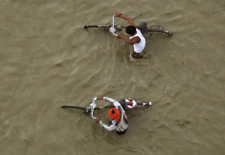 Men push their bicycles through the flooded banks of the river Ganges after heavy rains in Allahabad, India, July 16, 2015. REUTERS/Jitendra Prakash/Files