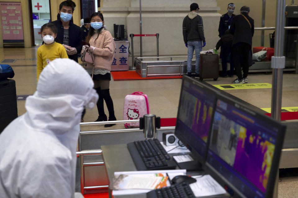 Passengers wearing face masks to protect against the spread of new coronavirus watch as a worker in a protective suit monitors a temperature scanner at Hankou train station after of the resumption of train services in Wuhan in central China's Hubei Province, Wednesday, April 8, 2020. After 11 weeks of lockdown, the first train departed Wednesday morning from a re-opened Wuhan, the origin point for the coronavirus pandemic, as residents once again were allowed to travel in and out of the sprawling central Chinese city. (AP Photo/Ng Han Guan)