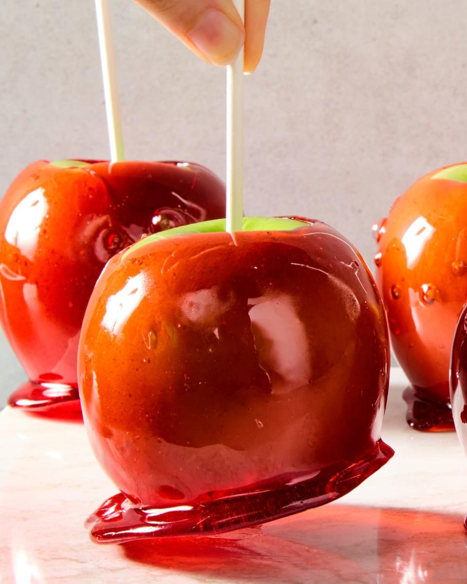 green apples with a red candy coating and a popsicle stick