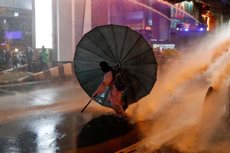 A man takes cover behind an umbrella during an anti-government protest, in Bangkok